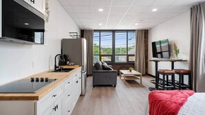 A modern hotel room with a kitchenette, a sofa, a dining area, and a bed.