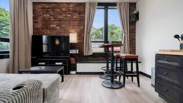 A modern room with a brick wall, a TV, a sofa, a dining table with stools, and a wooden cabinet.