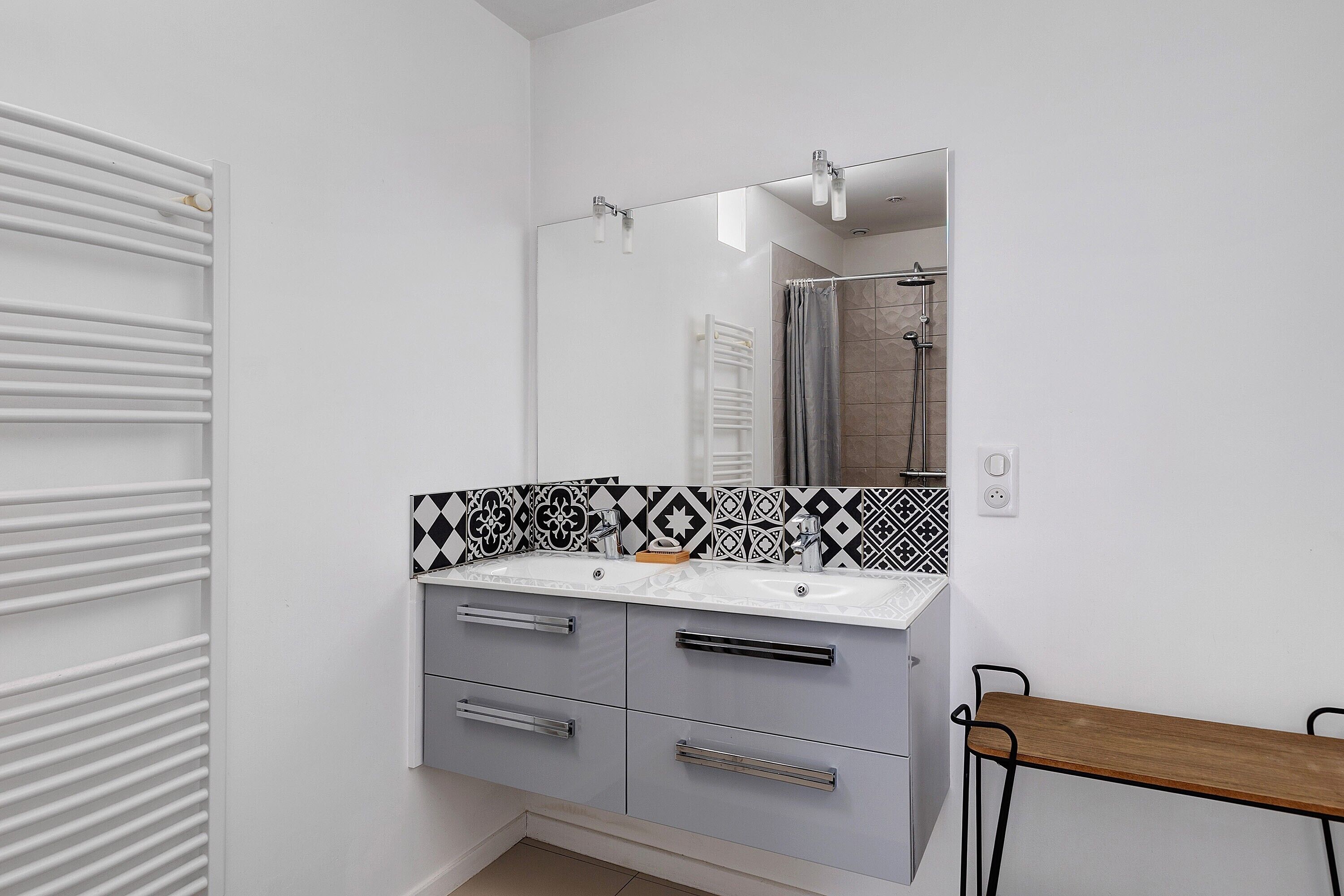 Een badkamer met een witte wastafel, een spiegel, een douche en een houten bankje.