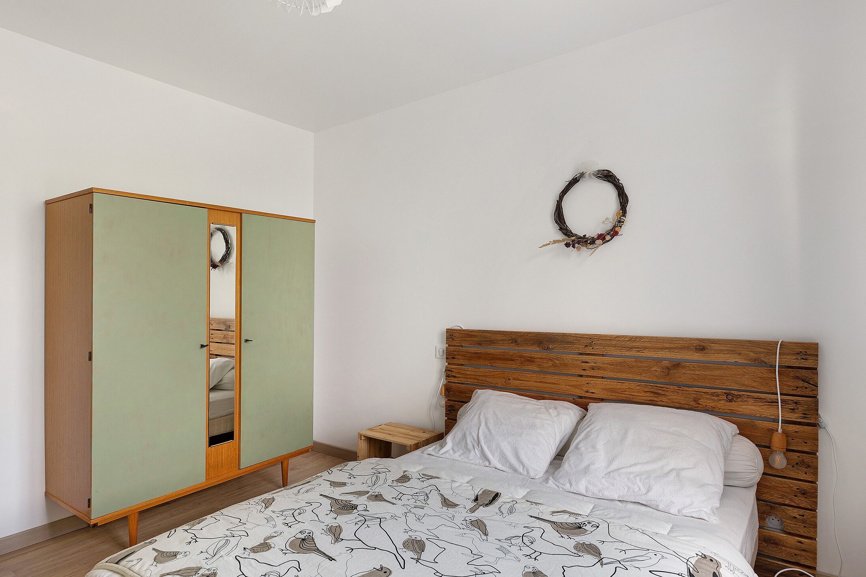 Ein Schlafzimmer mit Bett, Kleiderschrank, Nachttisch und Wandleuchte.