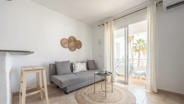A modern living room with a grey sofa, a small wooden table, a woven rug, and a wall-mounted decorative item. - A seaside retreat with swimming pool (Ciutadella)