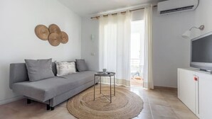 A modern living room with a grey sofa, a round woven rug, a small table, and a TV on a white cabinet. - A seaside retreat with swimming pool (Ciutadella)
