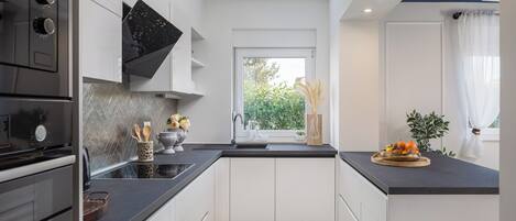 A modern kitchen with white cabinets, black countertops, and a window with a view of greenery.