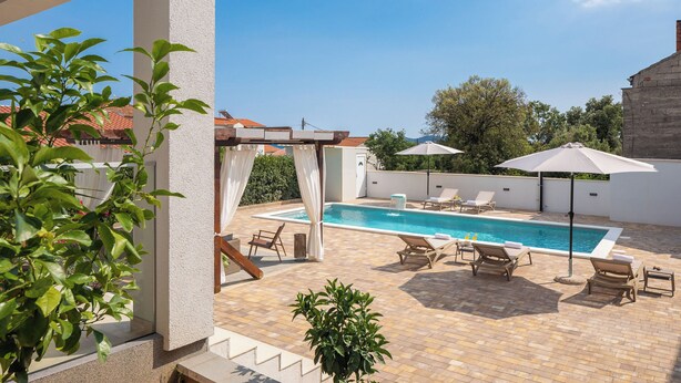A rooftop pool area with a clear blue pool, lounge chairs, and umbrellas. - Villa Peregrine (Pakostane)