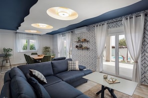 Un salon moderne avec un canapé bleu foncé, une table basse blanche et un coin repas comprenant une table et des chaises en bois.