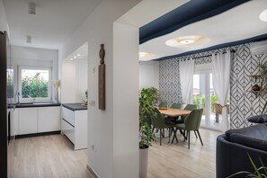 Una cocina moderna con armarios blancos y un comedor con mesa de madera y sillas verdes.