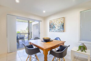 A dining area with a wooden table, black chairs, and a large bowl. There is a sliding glass door leading to an outdoor patio. - Spacious Flat With Parking & Dedicated EV Station (Batemans Bay)