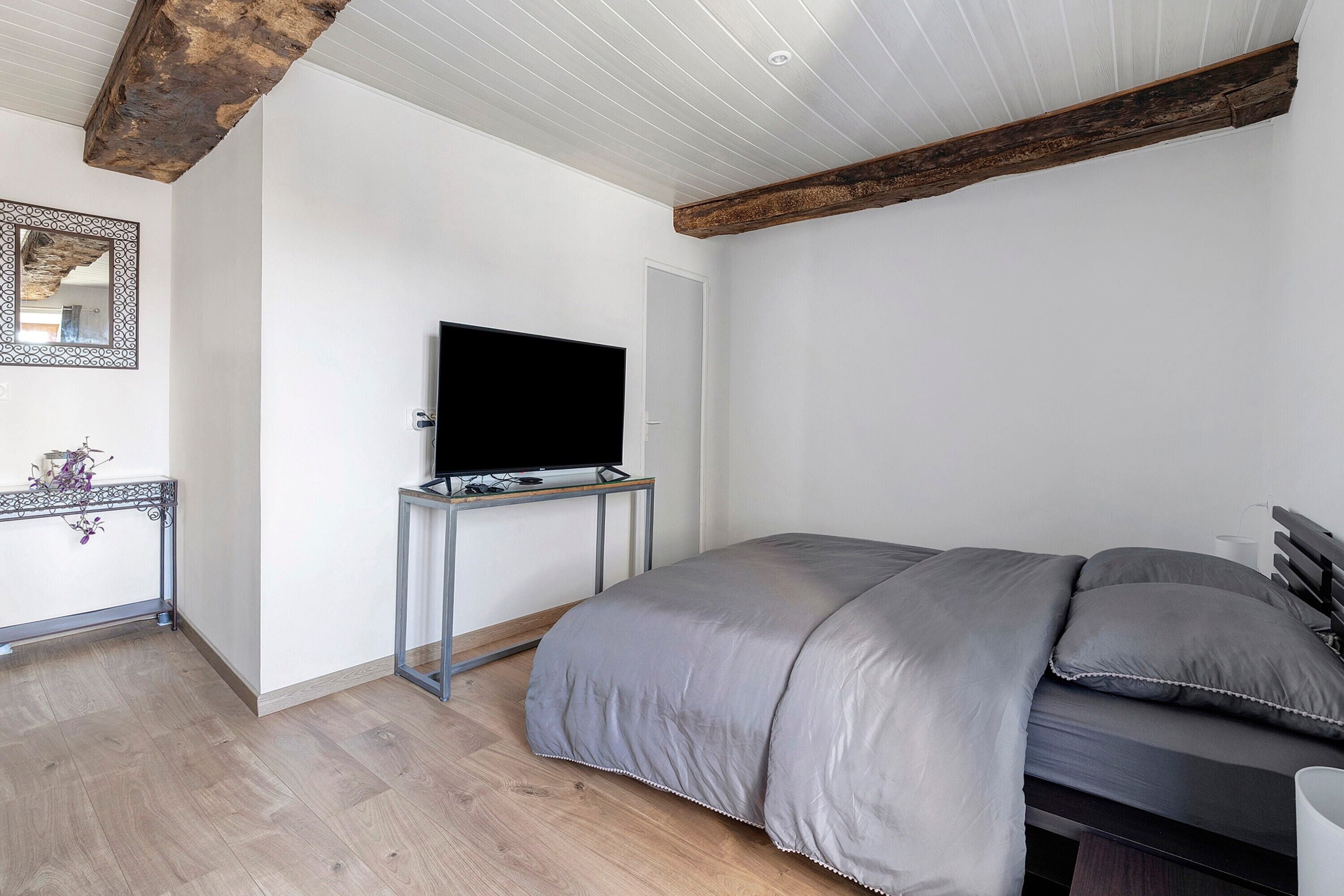 Un dormitorio con cama, televisor sobre un mueble, espejo y viga de techo de madera.
