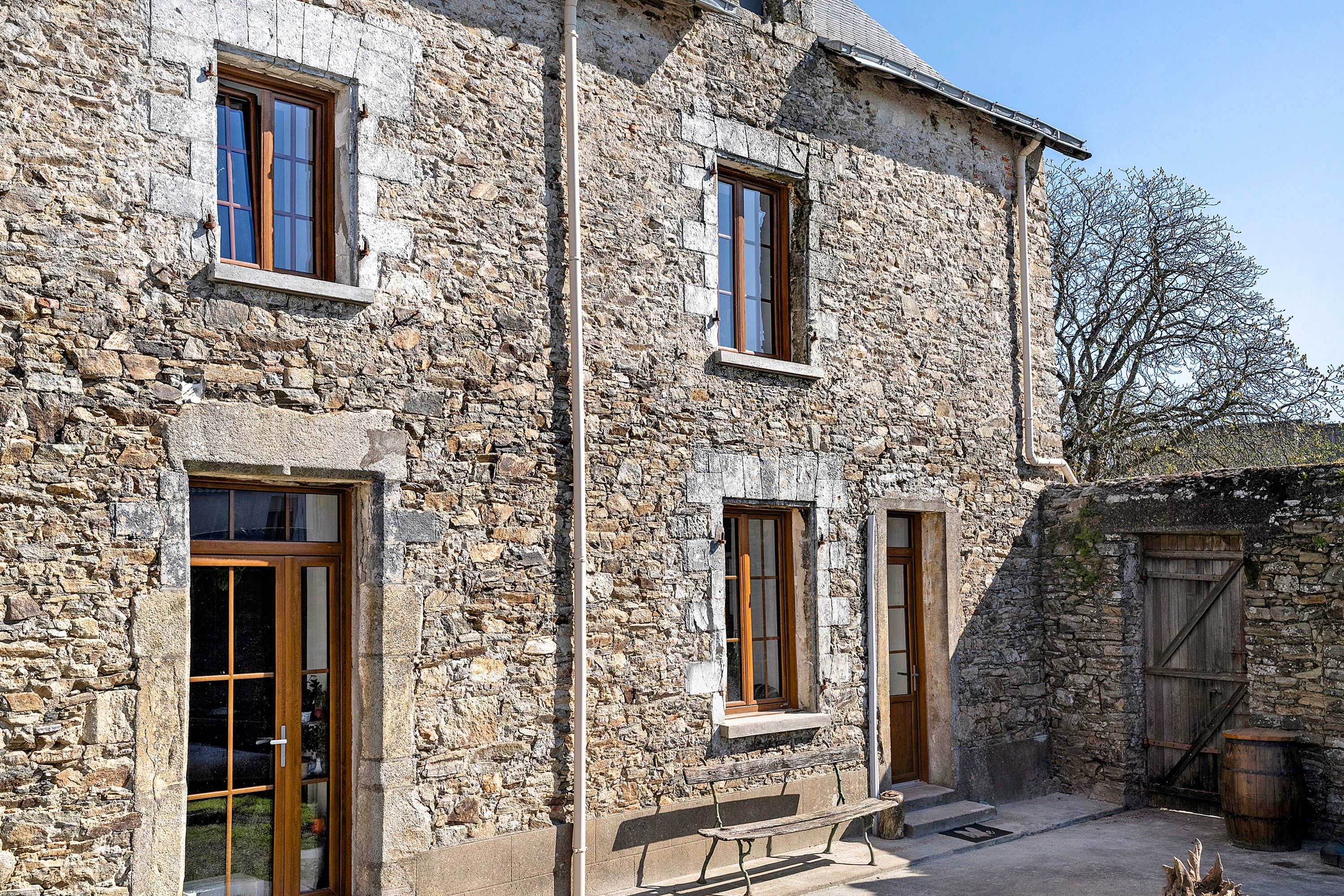 Un bâtiment en pierre doté de nombreuses fenêtres, d’une porte en bois et d’un banc à l’extérieur.