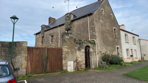 A historic stone building with a sloped roof, a wooden fence, and a parked car. - La Bohème Room 3 with Wi-Fi (Frossay)