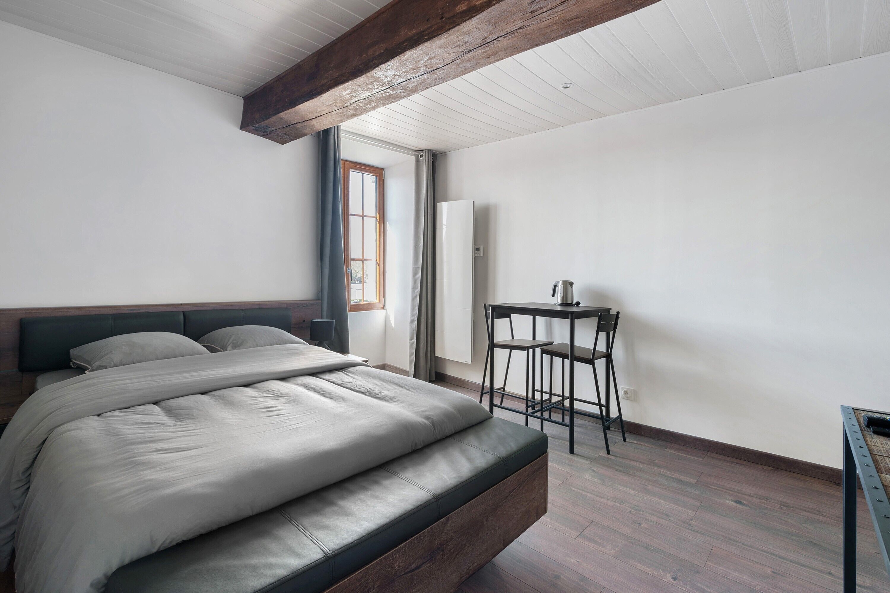A bedroom with a bed, a table with chairs, a window, and a door.