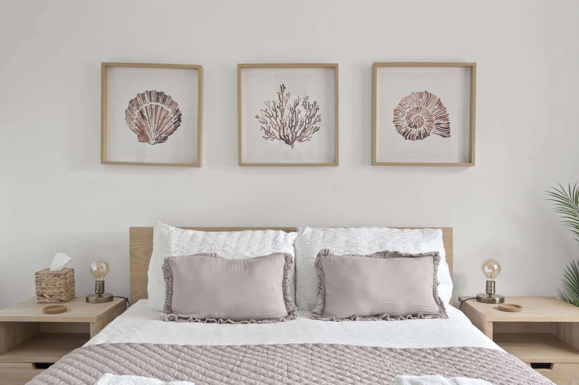 A bedroom with a bed, two bedside tables, and three framed wall art pieces.