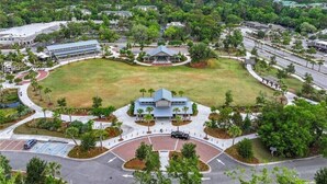 Vue aérienne d’un campus avec un bâtiment central entouré d’une zone verdoyante, de routes et d’un parking.