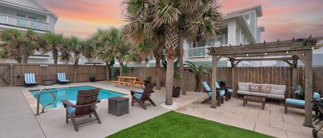 Your private oasis features a sparkling pool, covered lounge area, and tropical palms under dreamy sunset skies.