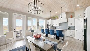 A modern kitchen with white cabinets, a wooden ceiling, and a dining area with a large table and blue chairs.