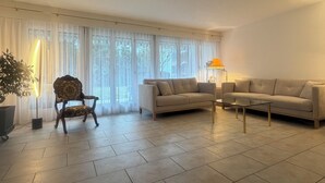 Un salon spacieux avec une grande fenêtre, un canapé, un fauteuil et une table basse.
