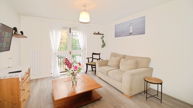 A living room with a sofa, a coffee table, a wooden dresser, a TV, and a painting of a lighthouse. - Stylish & Comfy | Near Canary Wharf | Self Check-In | WiFi (London)