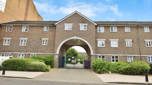 A multi-story brick building with a central archway entrance, surrounded by greenery and a paved walkway. - Stylish & Comfy | Near Canary Wharf | Self Check-In | WiFi (London)