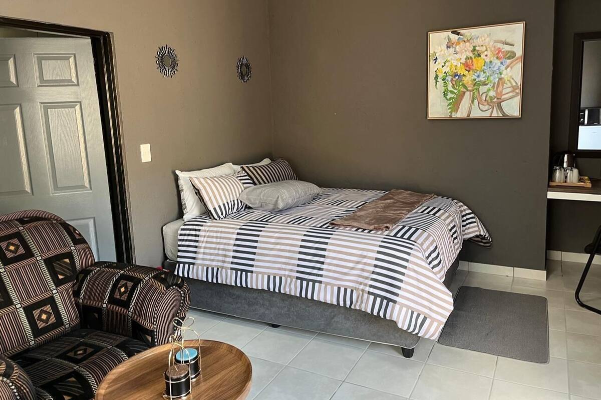 Un dormitorio con cama, una silla, una mesita y un cuadro en la pared.