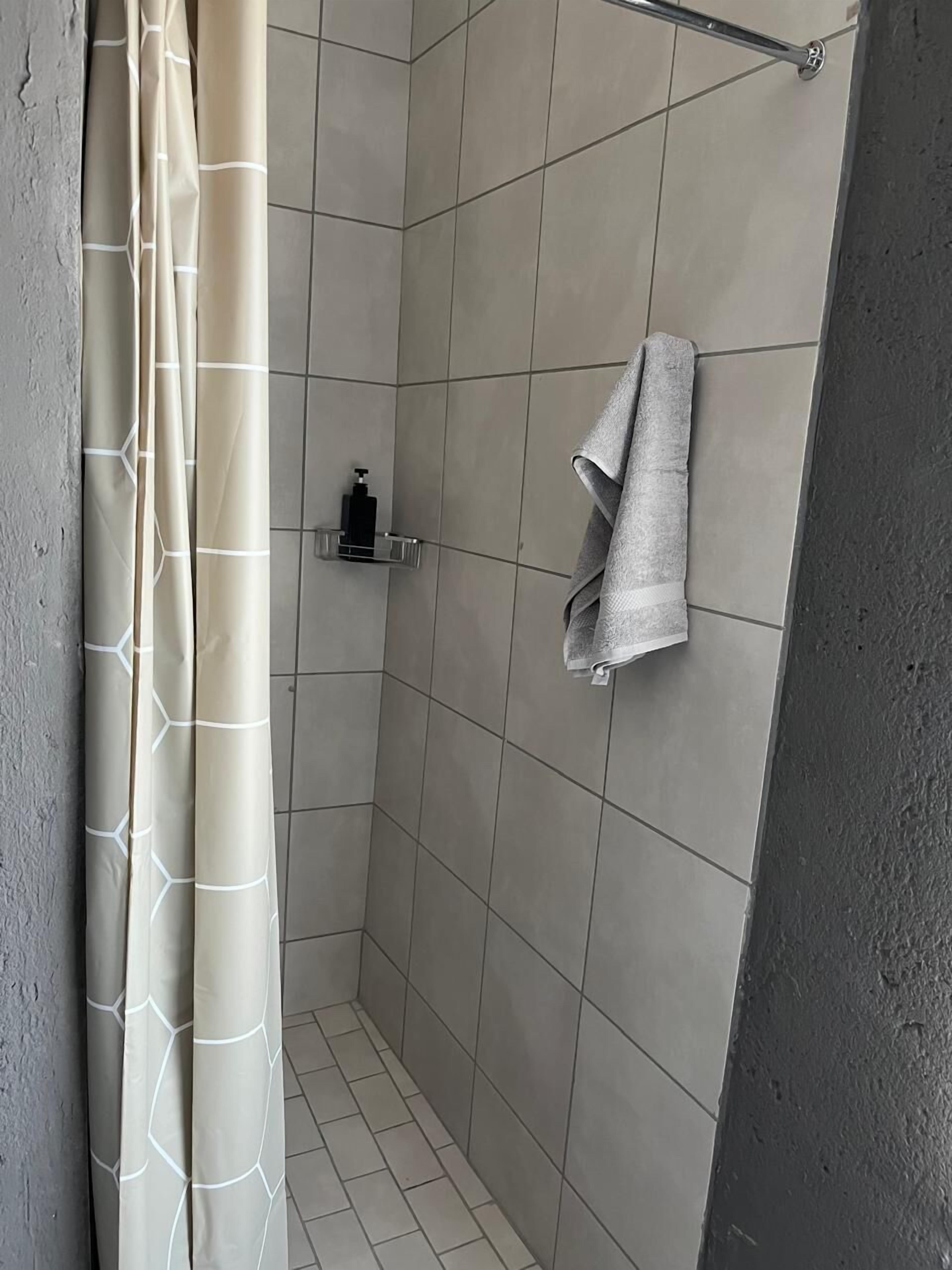 A small, tiled shower area with a shower curtain, a towel rack, and a soap dispenser.