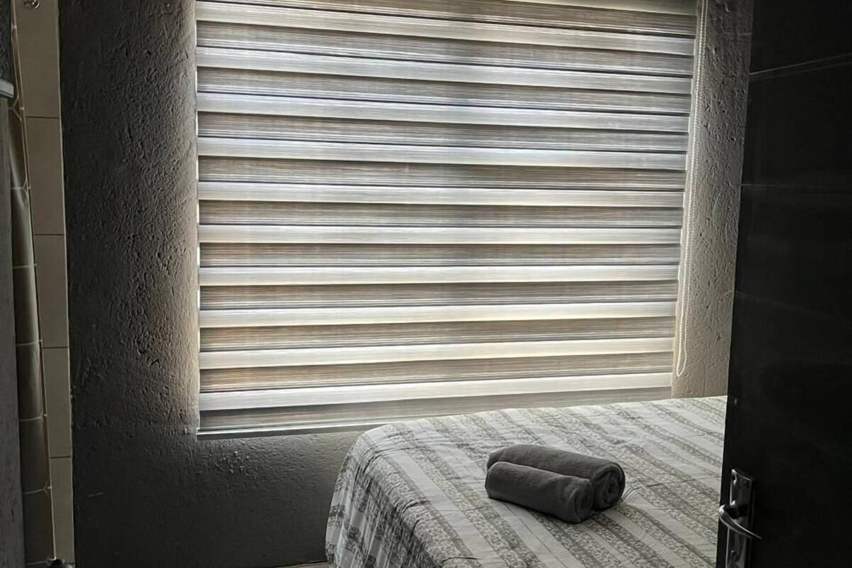 Un dormitorio con ventana, una cama con manta estampada, un hervidor y una puerta.