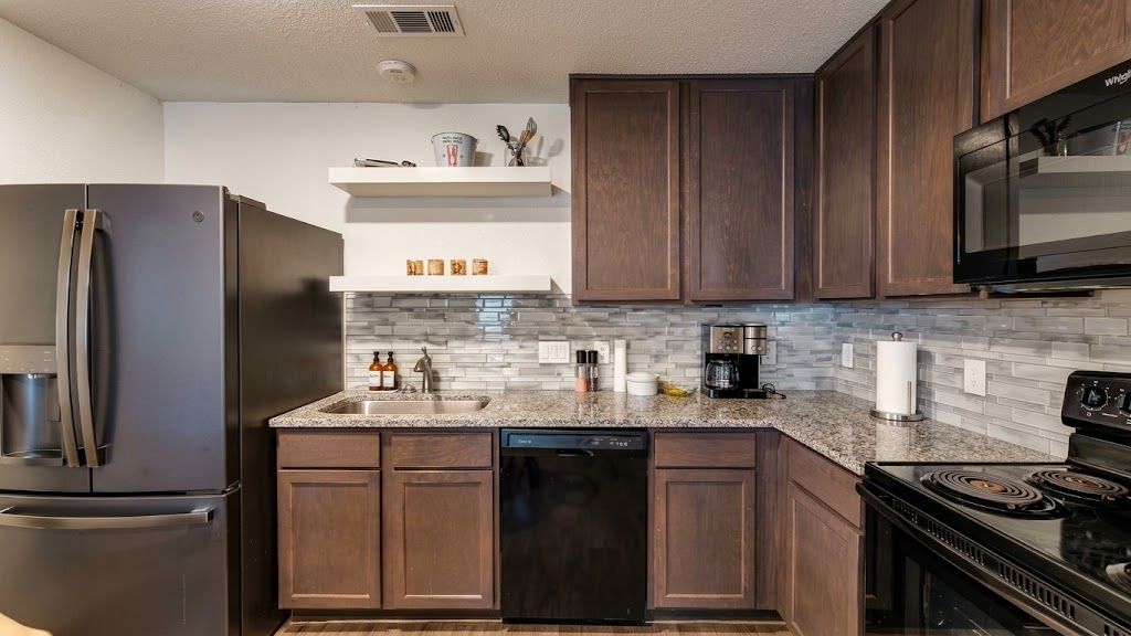A modern kitchen with dark wooden cabinets, a stainless steel refrigerator, a dishwasher, a stove, and a microwave.