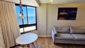 Un salón con un sofá gris, una mesa blanca y vistas al mar a través de un amplio ventanal.