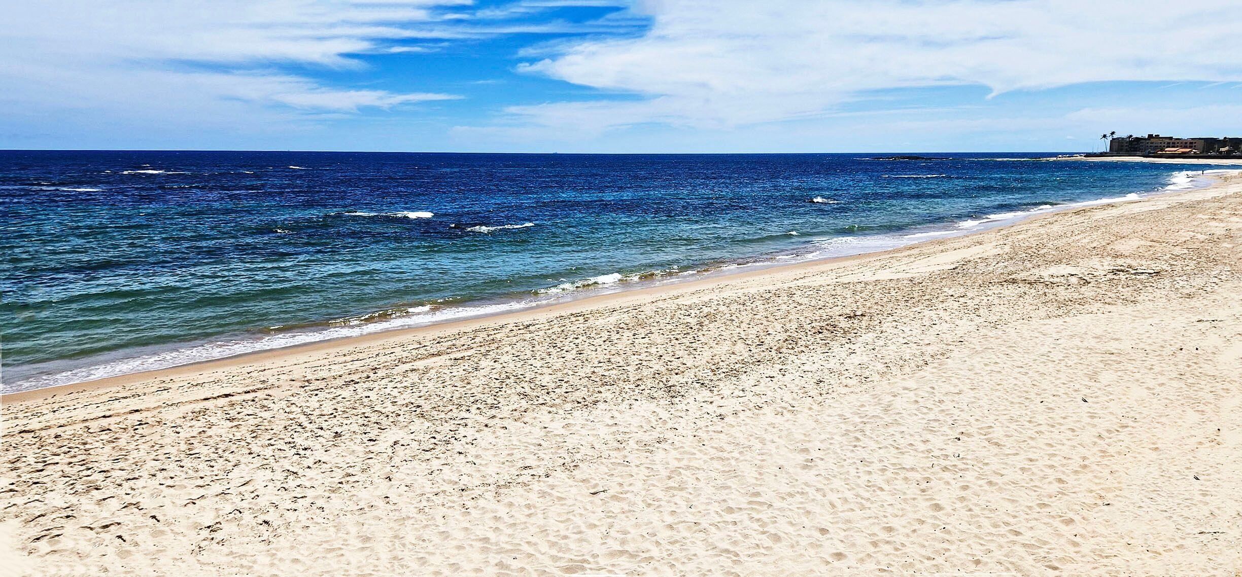 A beach with a clear view of the ocean and a distant building.