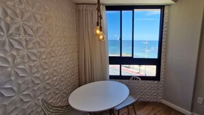 Una habitación con pared texturizada, una mesa redonda, una silla, una ventana con vista al mar y una lámpara colgante.