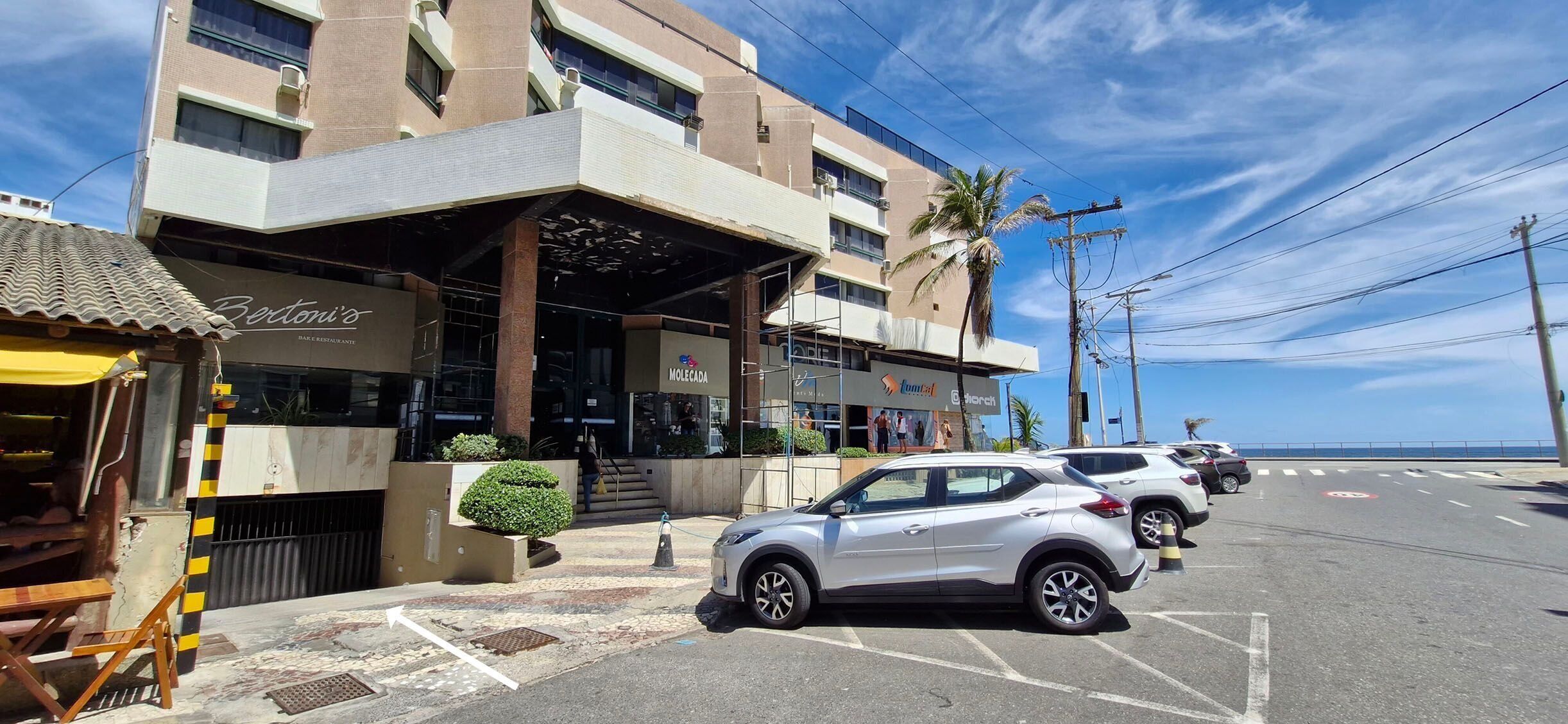 A hotel with a modern facade, a covered entrance, and a parking area with several cars.
