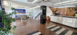 A modern hotel lobby with a reception desk, a staircase, a sofa, and decorative plants. - COPIT0108 - Condomínio Pituba Sol (Salvador)