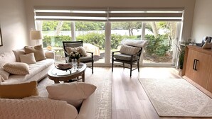 A spacious living room with a large window, a sofa, a chair, a coffee table, and a cabinet. - Whitney Breeze Longboat Key (Longboat Key)