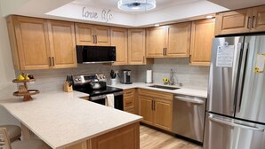 A modern kitchen with wooden cabinets, stainless steel appliances, and a central island with bar stools. - Whitney Breeze Longboat Key (Longboat Key)