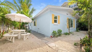 A white house with yellow shutters, a picnic table, and a palm tree in the yard. - Blue Sky Day Beach Cottage (Anna Maria)