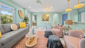 A living room with a sofa, ottoman, and chairs, a ceiling fan, and a dining area with a table and chairs. - Blue Sky Day Beach Cottage (Anna Maria)