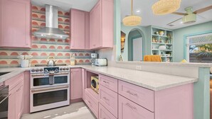 A kitchen with pink cabinets, a white stove, and a teal accent wall. - Blue Sky Day Beach Cottage (Anna Maria)