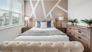 A bedroom with a large bed, two bedside tables, a wooden dresser, and a window with blinds. - Magical and Cozy 3BR Family Home Near Disney, with Private Pool, Games & BBQ. (Clermont)