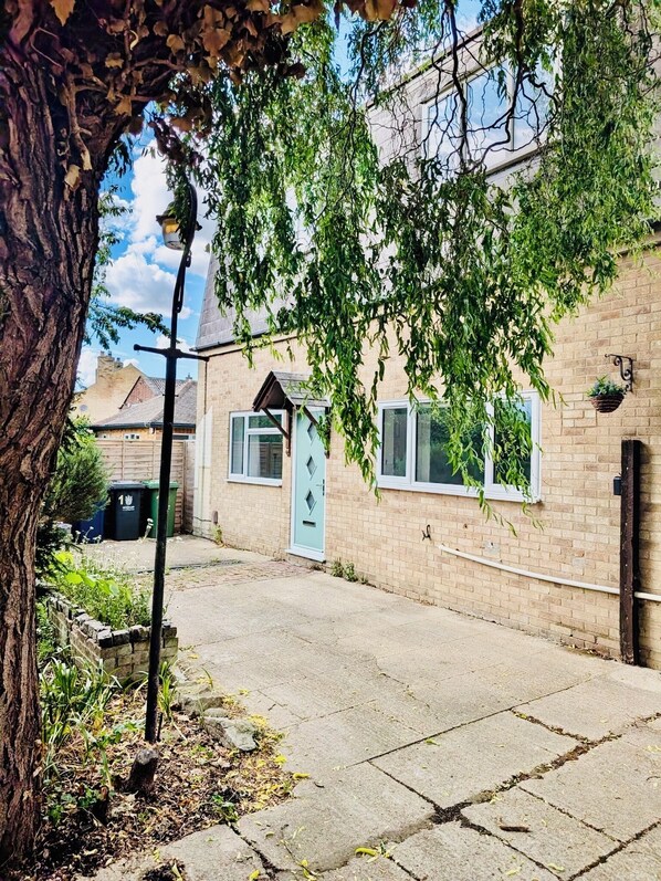 A residential street with a brick house, a tree, and a hanging plant. - Willow Cottage - 2 Bed Flat on charming village Green 5 miles from Cambridge. (Rampton)