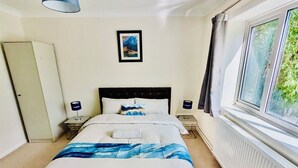 Un dormitorio con cama, ventana, radiador, un cuadro en la pared y una puerta.