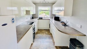 Una cocina compacta con armarios blancos, piso de baldosas de piedra y vista por una ventana.