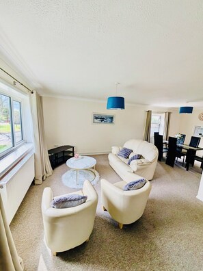 A living room with a sofa set, a coffee table, a dining table with chairs, and a blue pendant light. - Willow Cottage - 2 Bed Flat on charming village Green 5 miles from Cambridge. (Rampton)