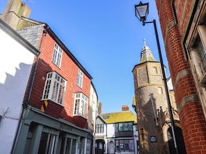 A narrow street with red brick buildings, a tower with a clock, and a shop named 'WYLDER'. - 5B Bridge Street (Lyme Regis)