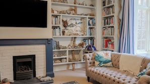 A living room with a fireplace, a sofa, a coffee table, and bookshelves filled with books and decorative items. - 5B Bridge Street (Lyme Regis)