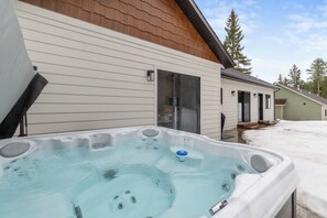 Un jacuzzi frente a una casa con puerta corrediza y suelo cubierto de nieve.