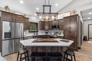 Une cuisine moderne dotée d’un îlot central, d’appareils électroménagers en acier inoxydable, de meubles en bois et d’un luminaire suspendu.