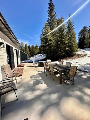 Un patio al aire libre con una mesa y sillas, rodeado de nieve y árboles.