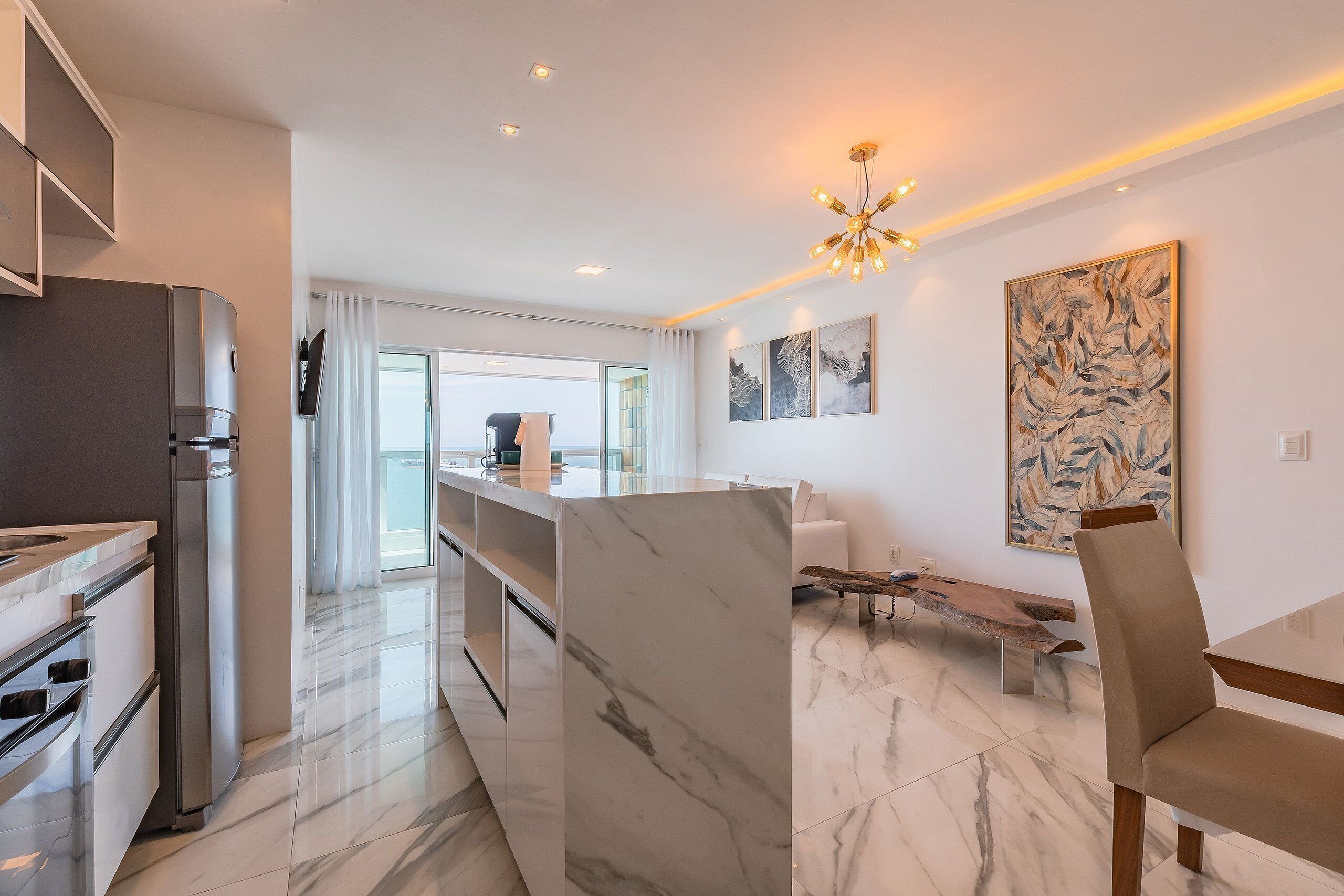 A modern kitchen with a built-in oven and refrigerator, a marble countertop, and a dining area with a bench and chair.