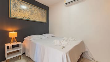 A hotel room with a bed, a bedside lamp, a wall-mounted air conditioner, and a large decorative piece above the bed.