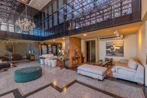 A spacious lobby with a high ceiling, a chandelier, a staircase, and a large window overlooking the interior. - Iracema Residence #1408 - Fortaleza by Carpediem (Fortaleza)