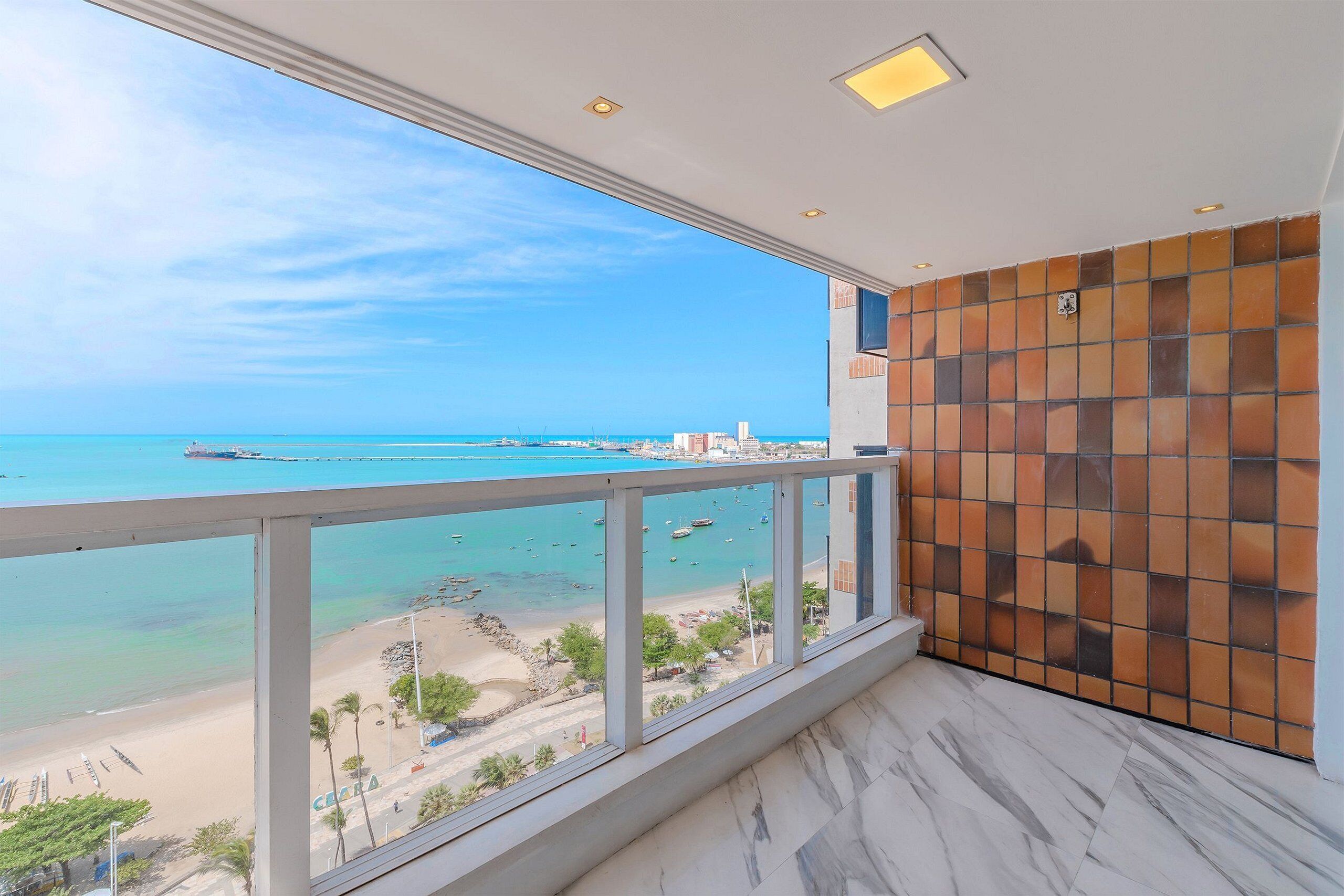 Ein Balkon mit Blick auf Strand und Meer, eine Kachelwand und ein Marmorboden.